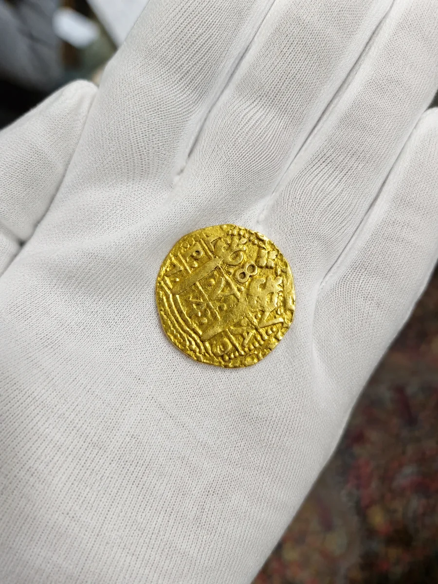 Revisión de moneda antigua de oro con guante blanco antes de decidir dónde venderla